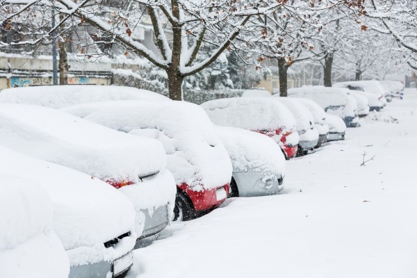 Cars covered in snow on a parking lot in the residential area during December snowfall